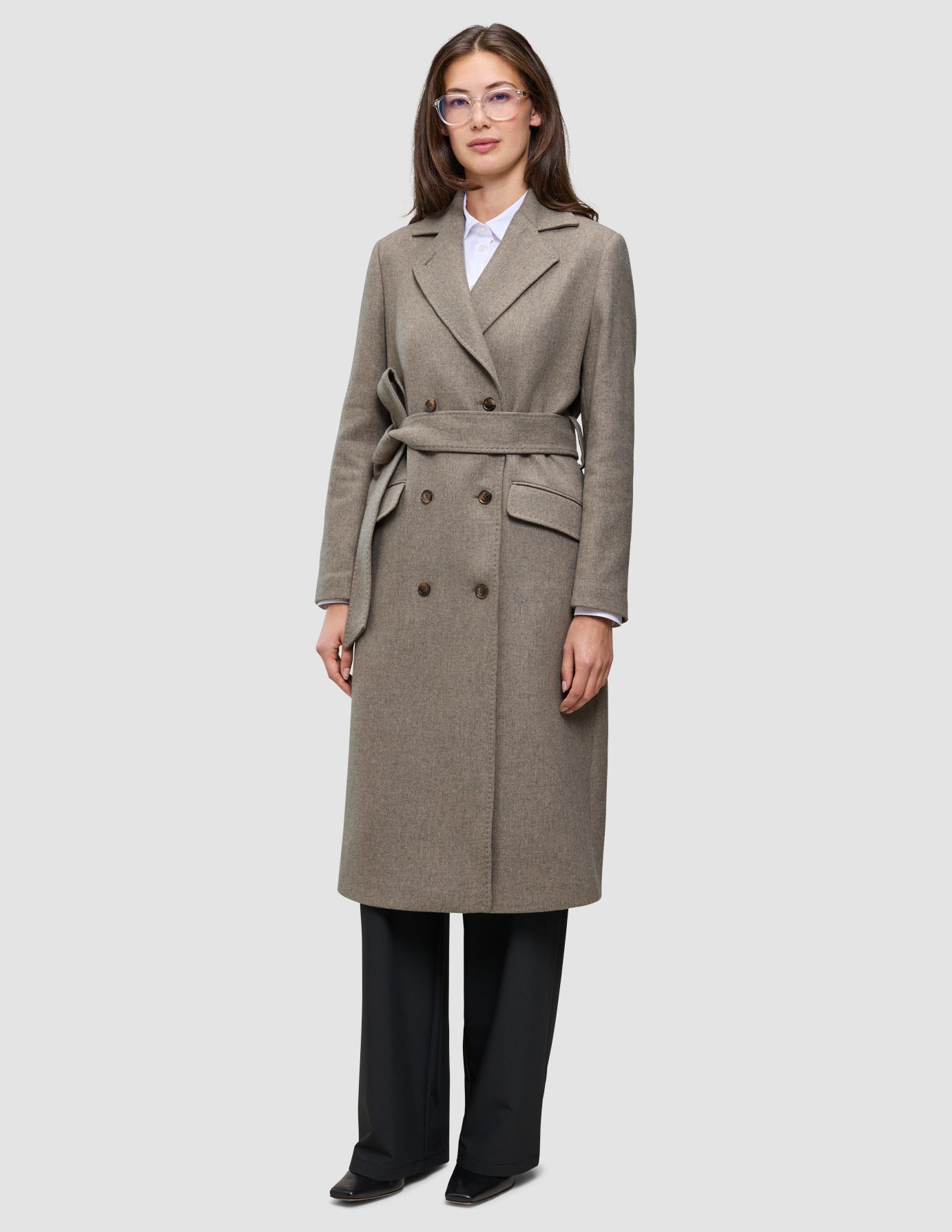 En kvinde iført en Women Wool Coat Greige – en knælang uldfrakke med dobbeltradet knaplukning og et matchende bindebælte.
