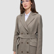 En kvinde har en Women Wool Coat Greige på – en lys brun-grå uldfrakke med dobbeltradet knapning – over en hvid skjorte med krave.