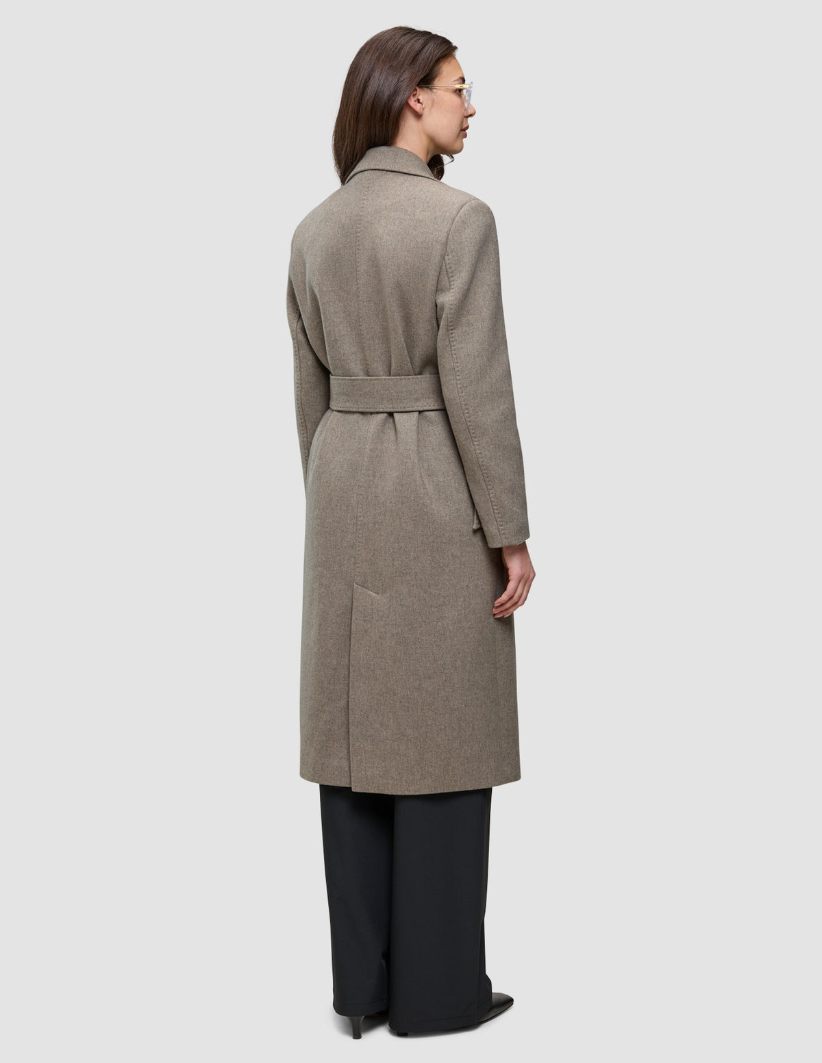 En gråbrun uldfrakke til kvinder i knælængde med bælte, slids bagpå og klassisk dansk design.